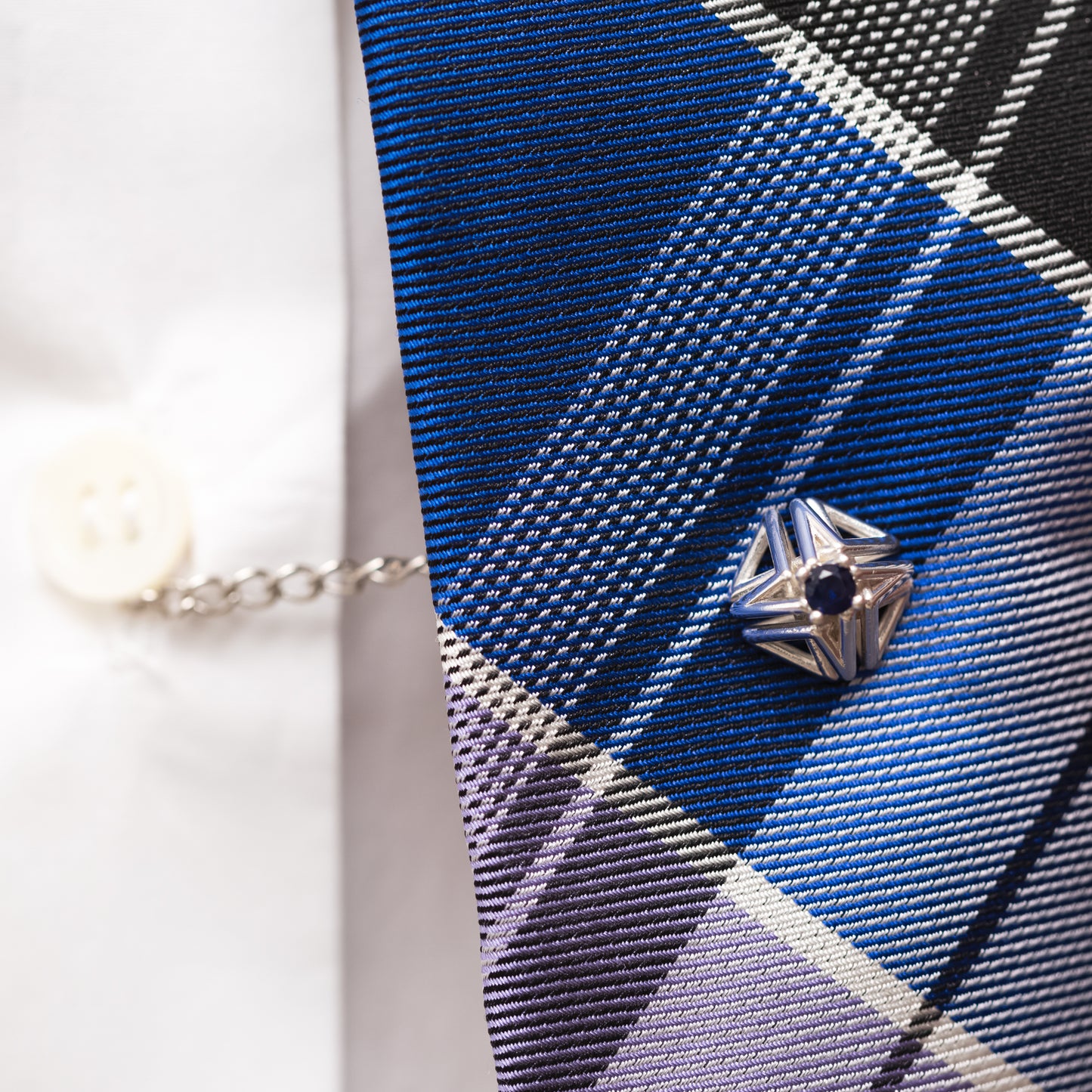 Blue sapphire and solid sterling silver tie tack worn with a blue plaid tie and white button down shirt. The tie tack���s security chain keeps the tie centered over the button placket, a detail that helps make this unisex accessory fit for the modern dandy.