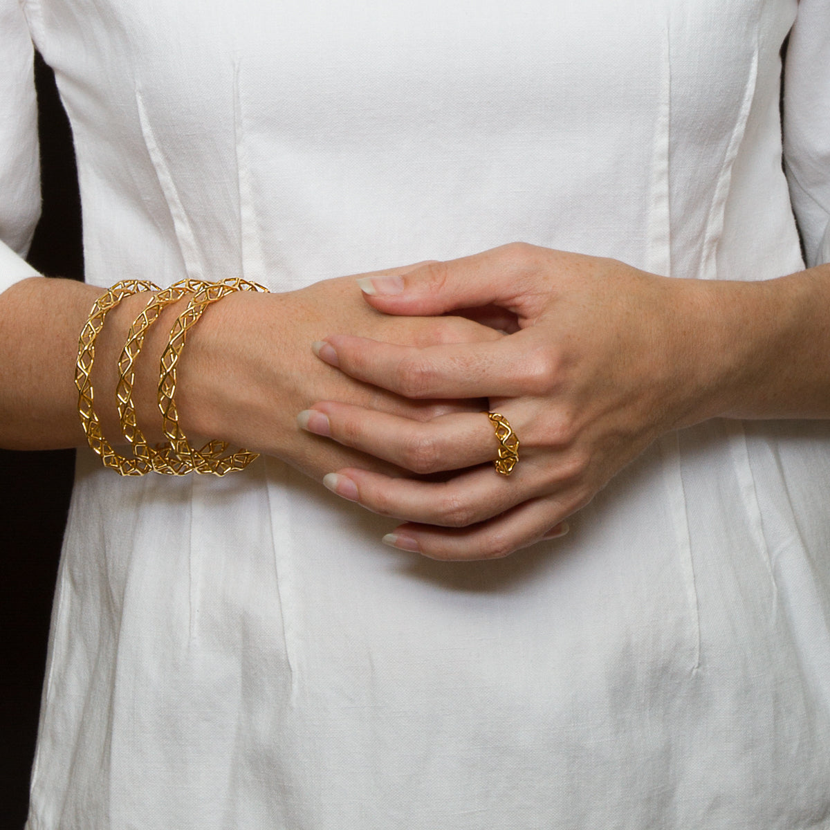 A person wearing three airy latticework bangle bracelets and a ring with matching architectural geometry.