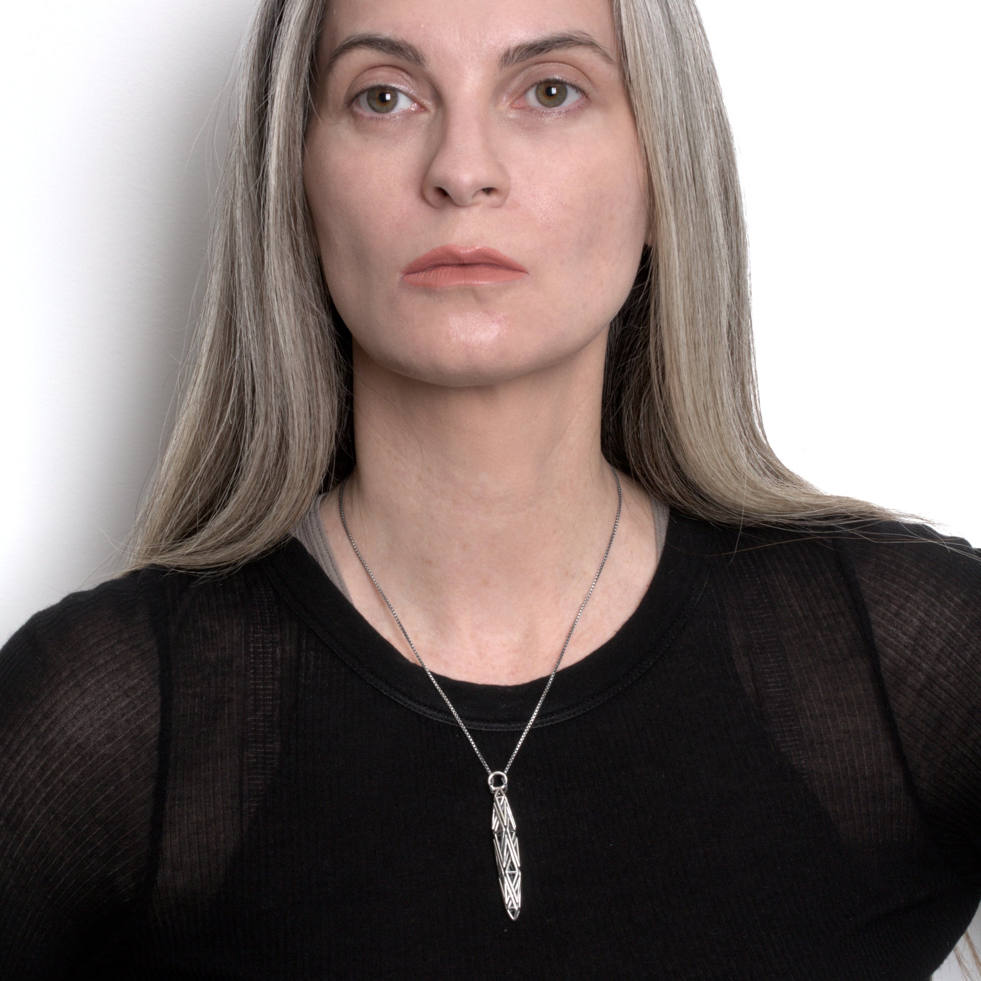 Woman in a black designer top wearing an angular geometric sterling silver pendant on a box chain, styled as a stark edgy look.