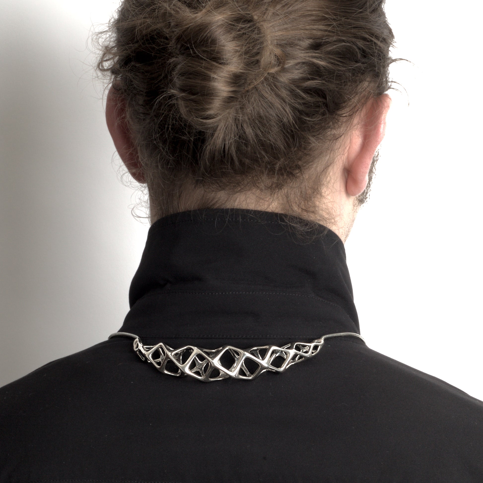 The solid sterling silver bolo tie���choker hybrid necklace styled on a man, with the necklace's geometric crest worn at the back of the shirt collar and the traditional bolo tie elements in front.