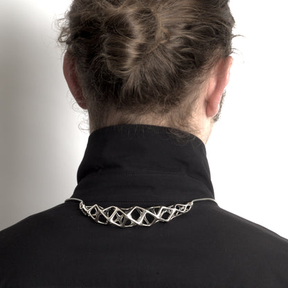 The solid sterling silver bolo tie���choker hybrid necklace styled on a man, with the necklace's geometric crest worn at the back of the shirt collar and the traditional bolo tie elements in front.