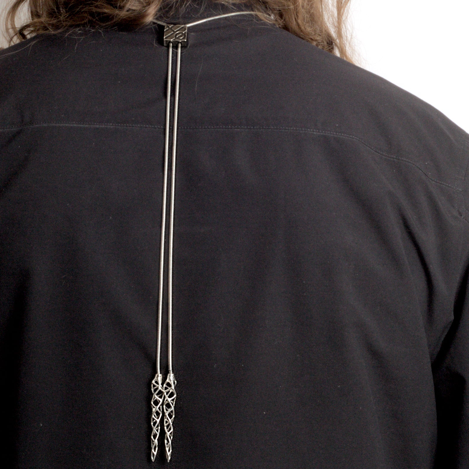 Back view of the .925 sterling silver choker/bolo-tie hybrid necklace worn by a man. In this image the bolo-tie tips hang down the man's back. 