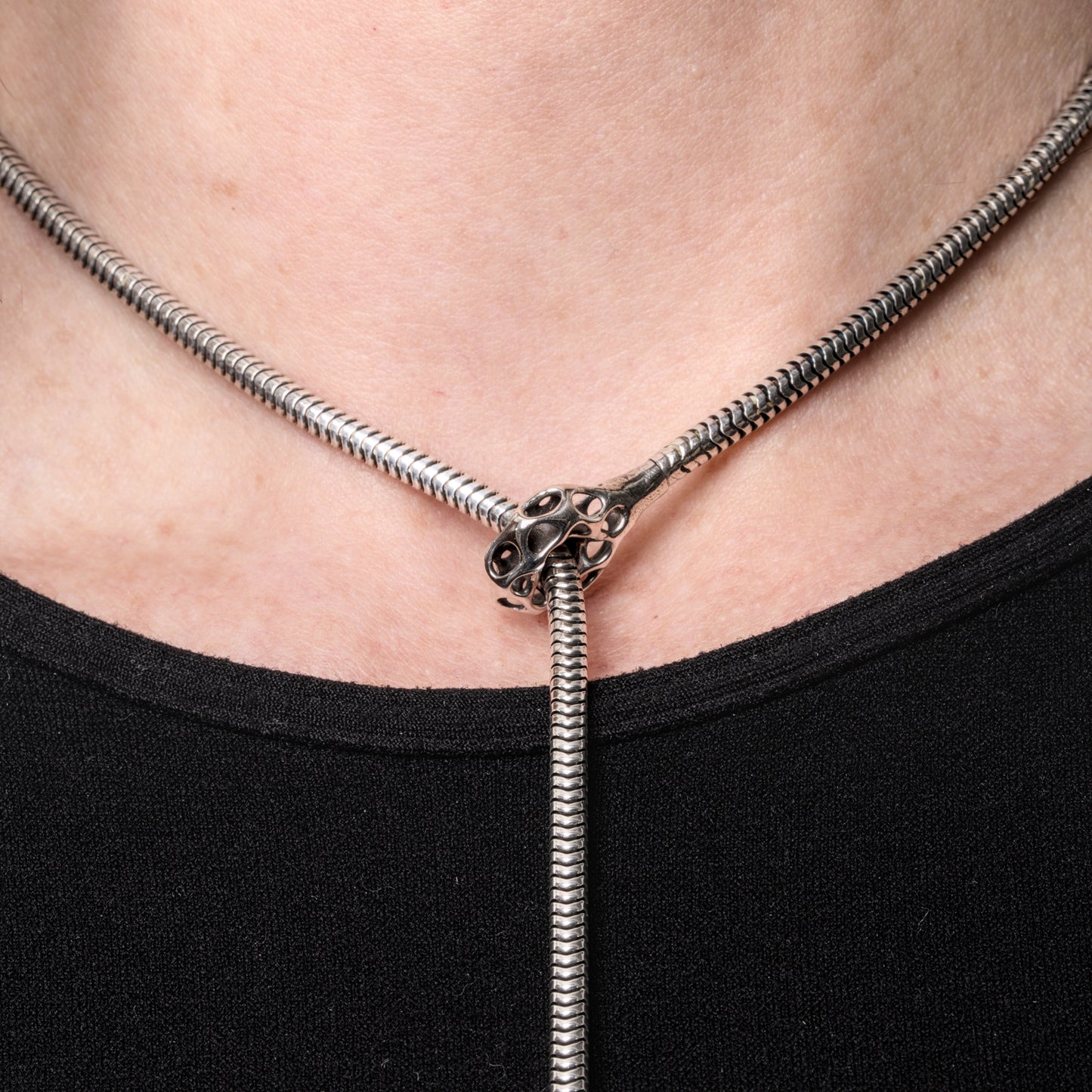Detail of a sterling silver lariat necklace with latticework cufflet closure worn close to the neck. The long snake chain lariat drapes comfortably down the body. 