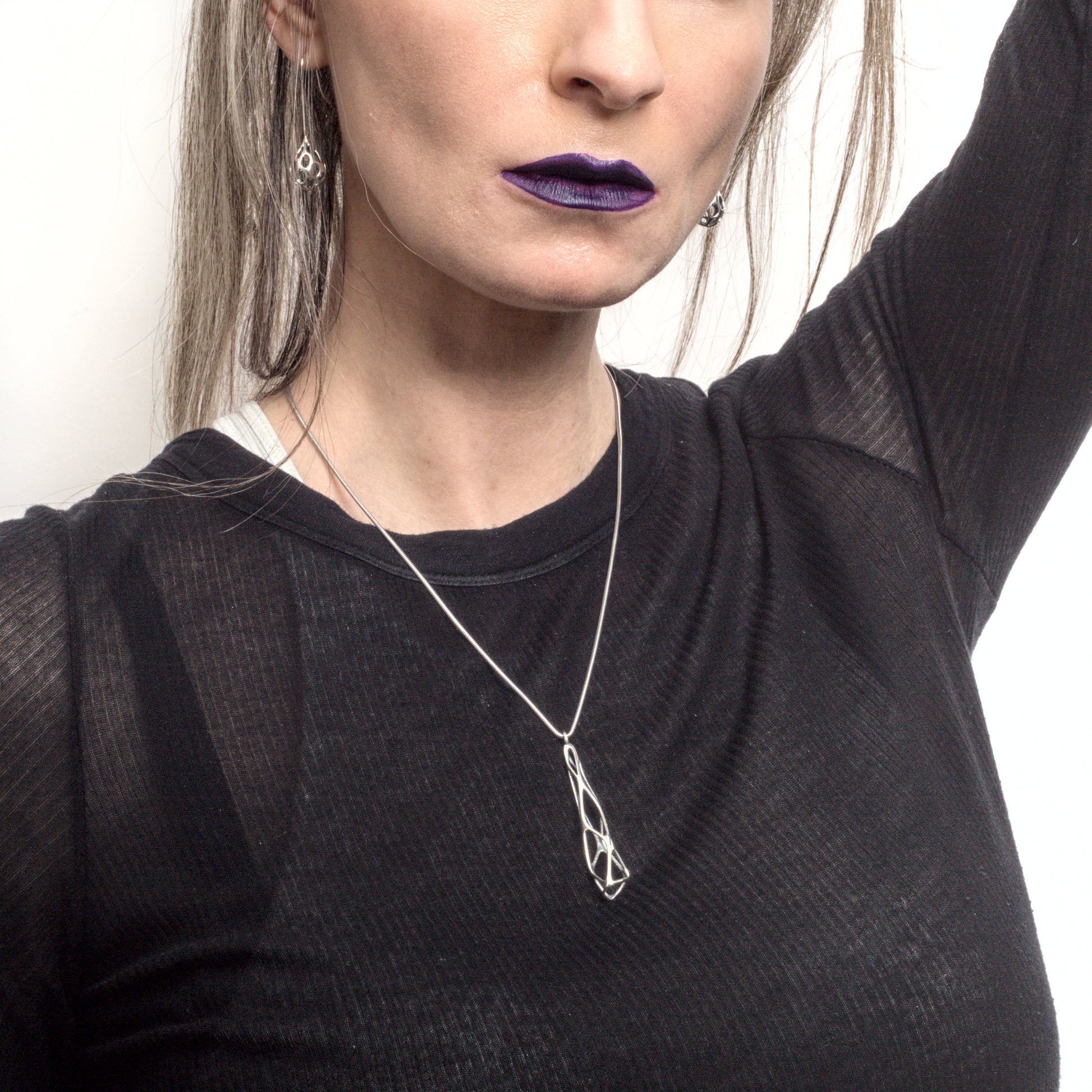 An edgy abstract sterling silver pendant necklace styled with a semi-sheer black designer t-shirt and dark lipstick. It's giving "elder goth".