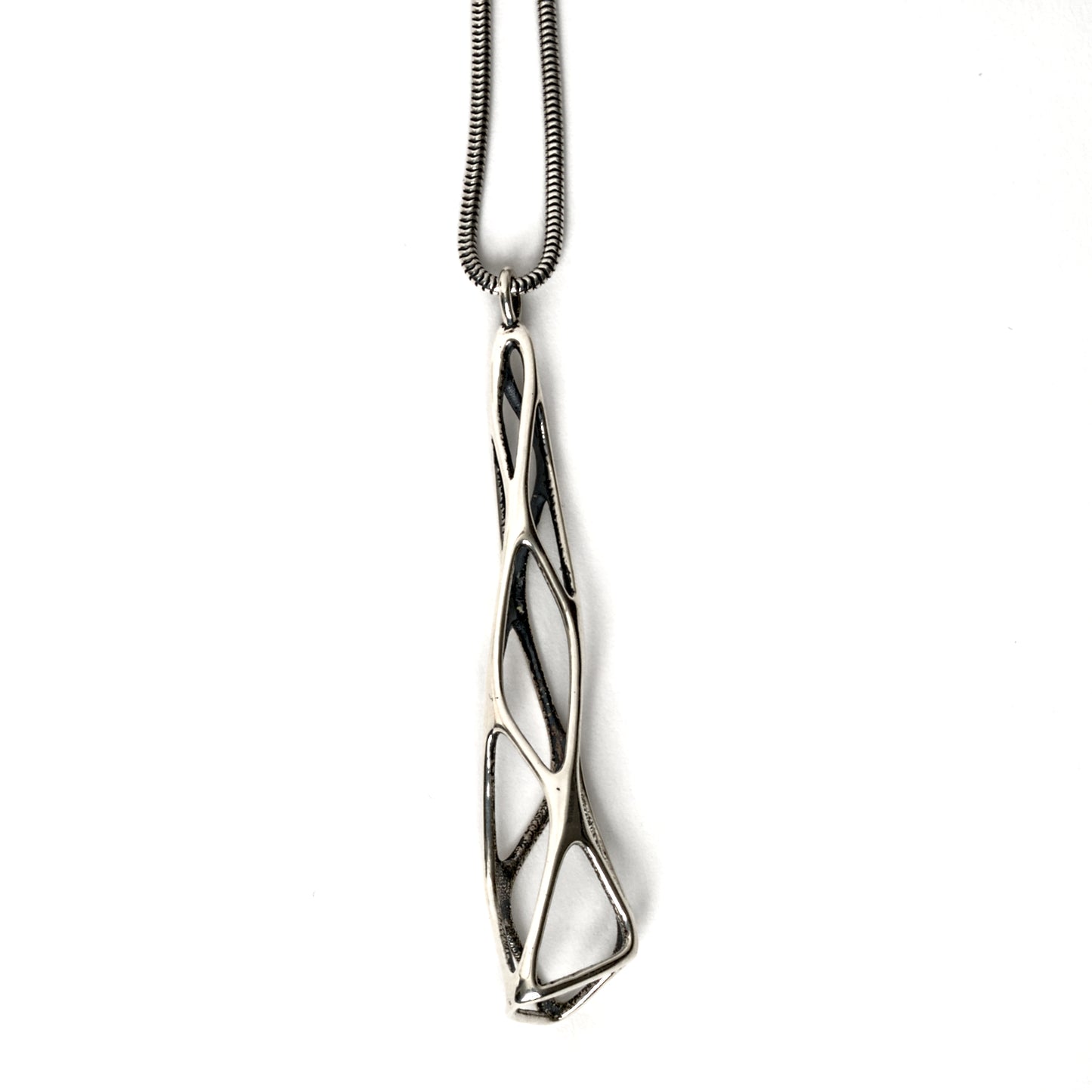 A contrast oxidized solid sterling silver elongated latticework pendant with outer surfaces polished to a mirror shine. The inner surfaces of this delicate lattice have a dark matte finish. The dimensional geometry is suspended from a matching snake chain. 
