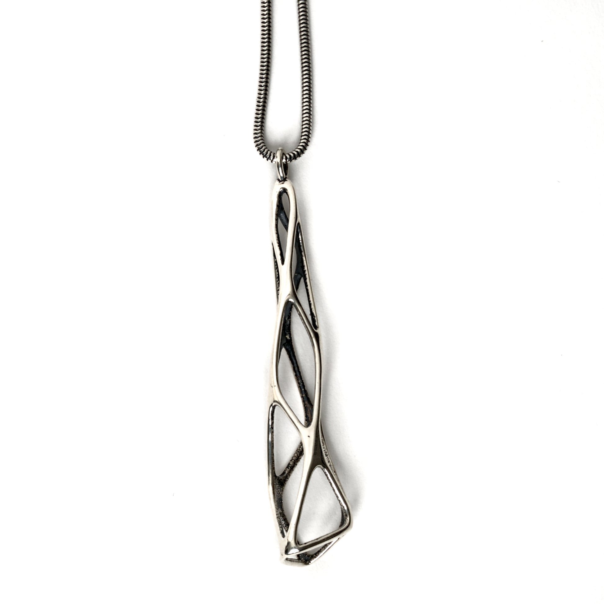A contrast oxidized solid sterling silver elongated latticework pendant with outer surfaces polished to a mirror shine. The inner surfaces of this delicate lattice have a dark matte finish. The dimensional geometry is suspended from a matching snake chain. 