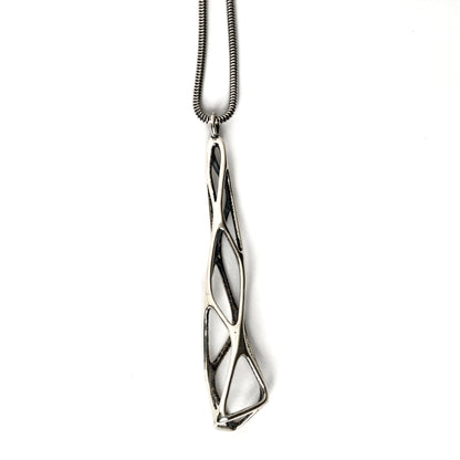 A contrast oxidized solid sterling silver elongated latticework pendant with outer surfaces polished to a mirror shine. The inner surfaces of this delicate lattice have a dark matte finish. The dimensional geometry is suspended from a matching snake chain. 