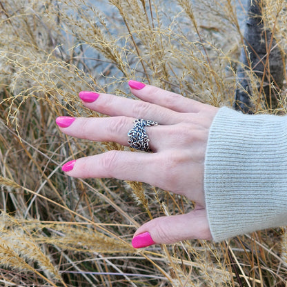 Hand with pink nails wearing a sterling silver graffiti ring against a winter wheat background. 