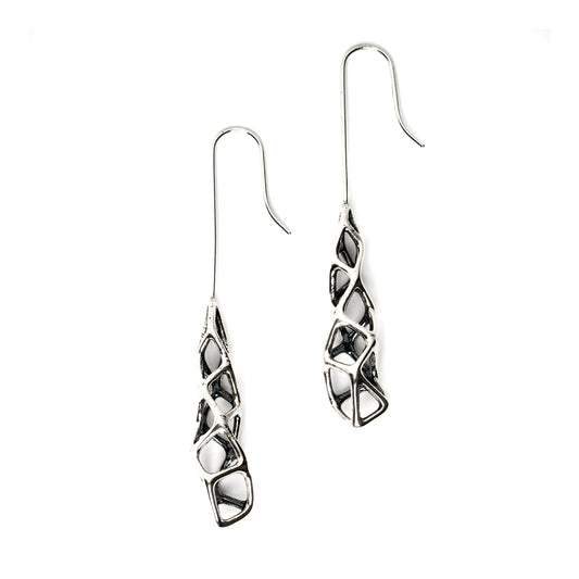 Edgy elongated drop earrings in solid sterling silver featuring dimensional geometric lattices with extreme contrast between blackened recesses and high polish outer surfaces. The dimensional design emphasizes vertical length, gravity, and unconventional elegance. 