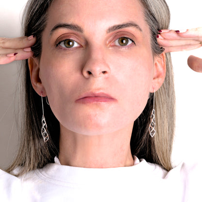 Solid sterling silver geometric lattice drop earrings are styled in this photo showing the symmetric and asymmetric properties of the dimensional designs. 
