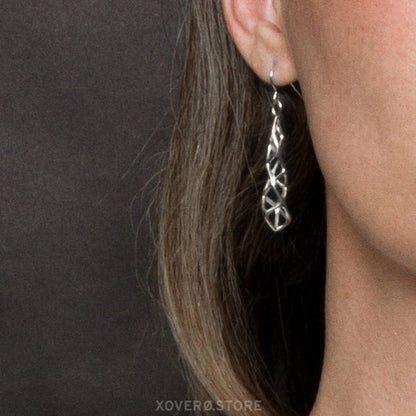 Close up of sterling silver spire shaped filigree dangle earring. The earrings hang from the earlobe to the jawline. 