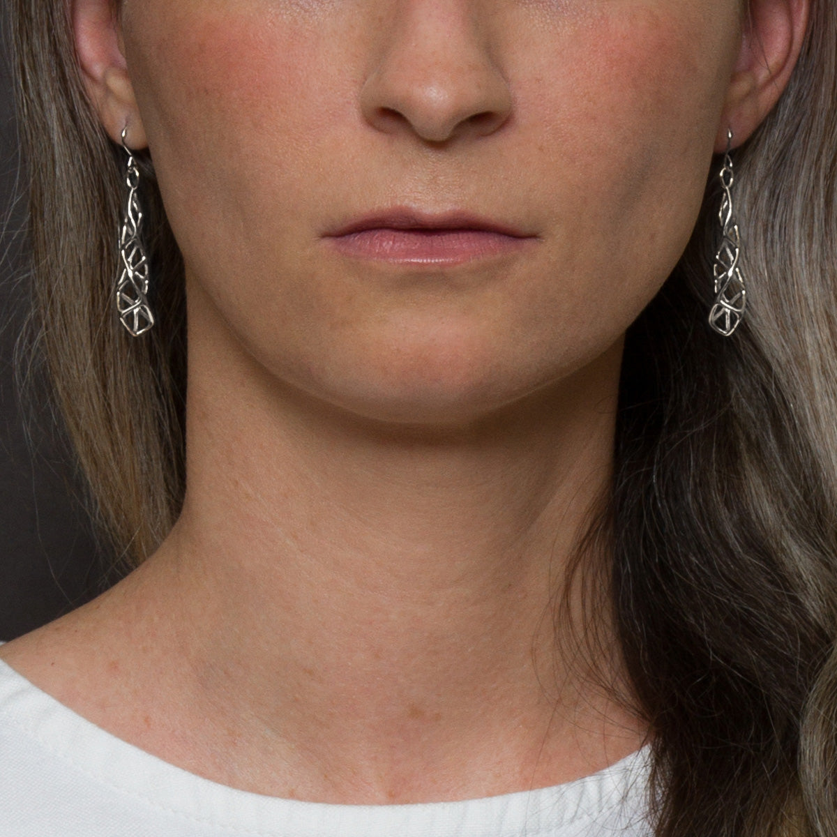 Sterling silver latticework earrings with angular geometric detail modeled by a woman. 