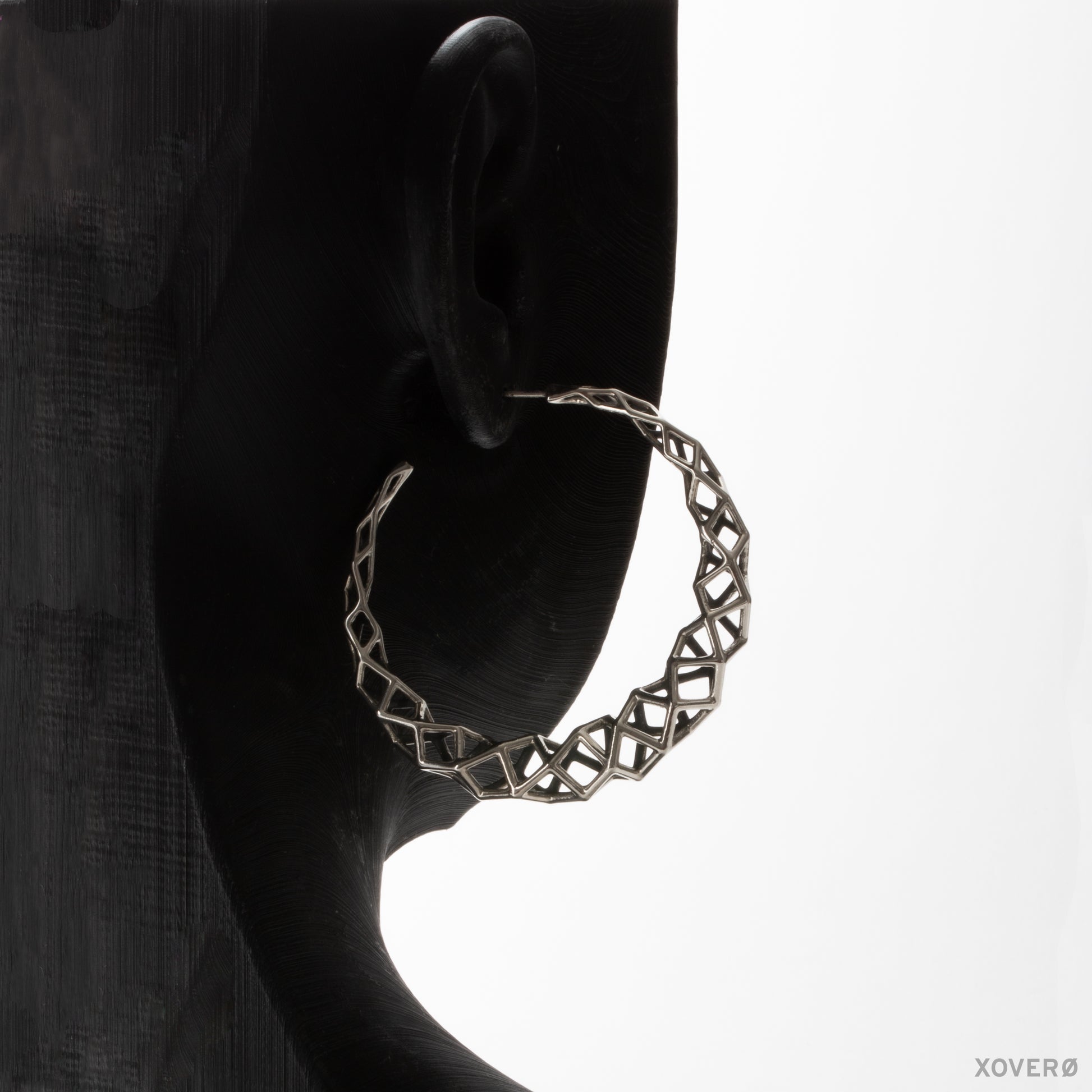 Close up of a sterling silver unconventional geometric hoop earring on a mannequin. The large latticework hoop makes a statement from all angles.