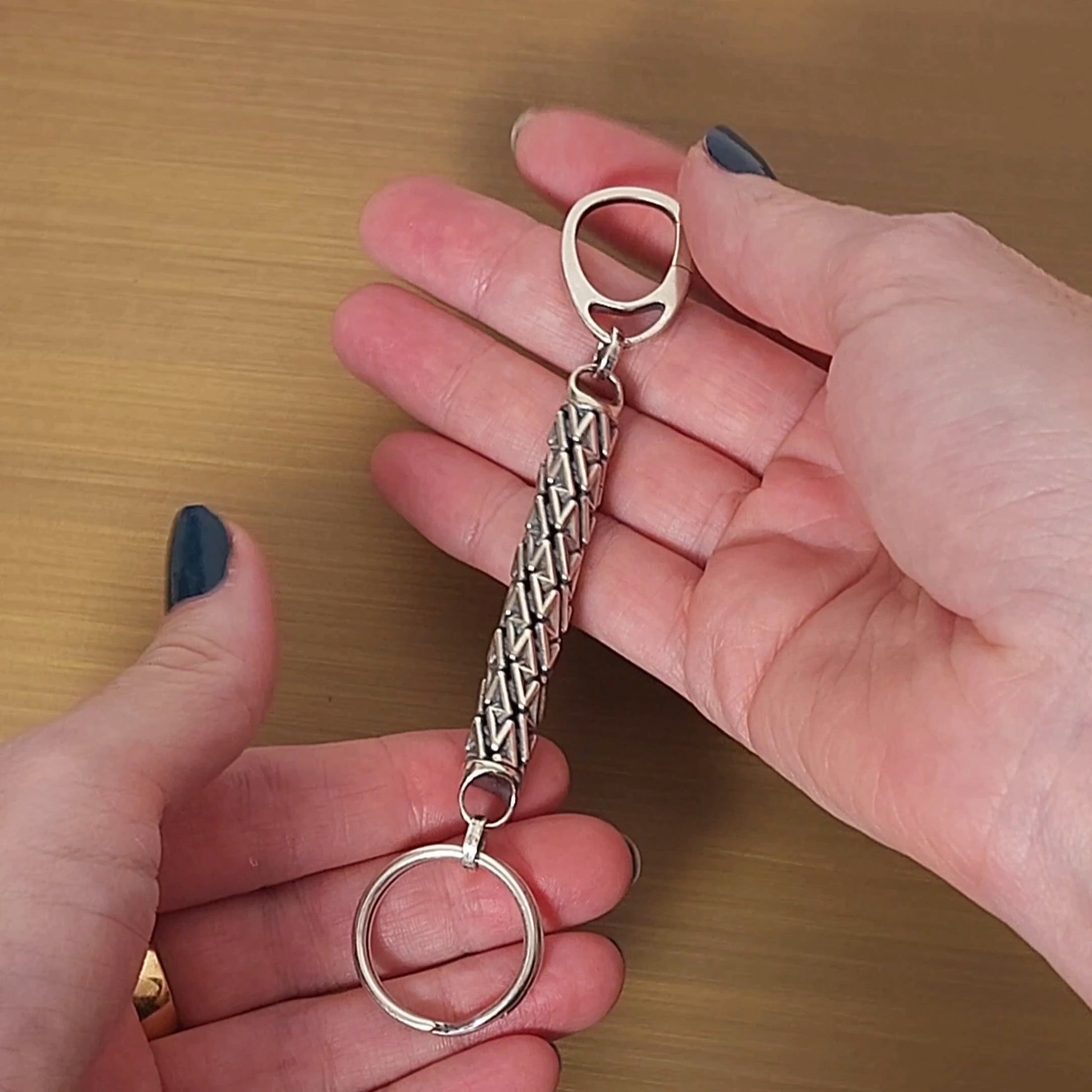 Geometric sterling silver designer keychain with precise dimensional details presented by female hands. 