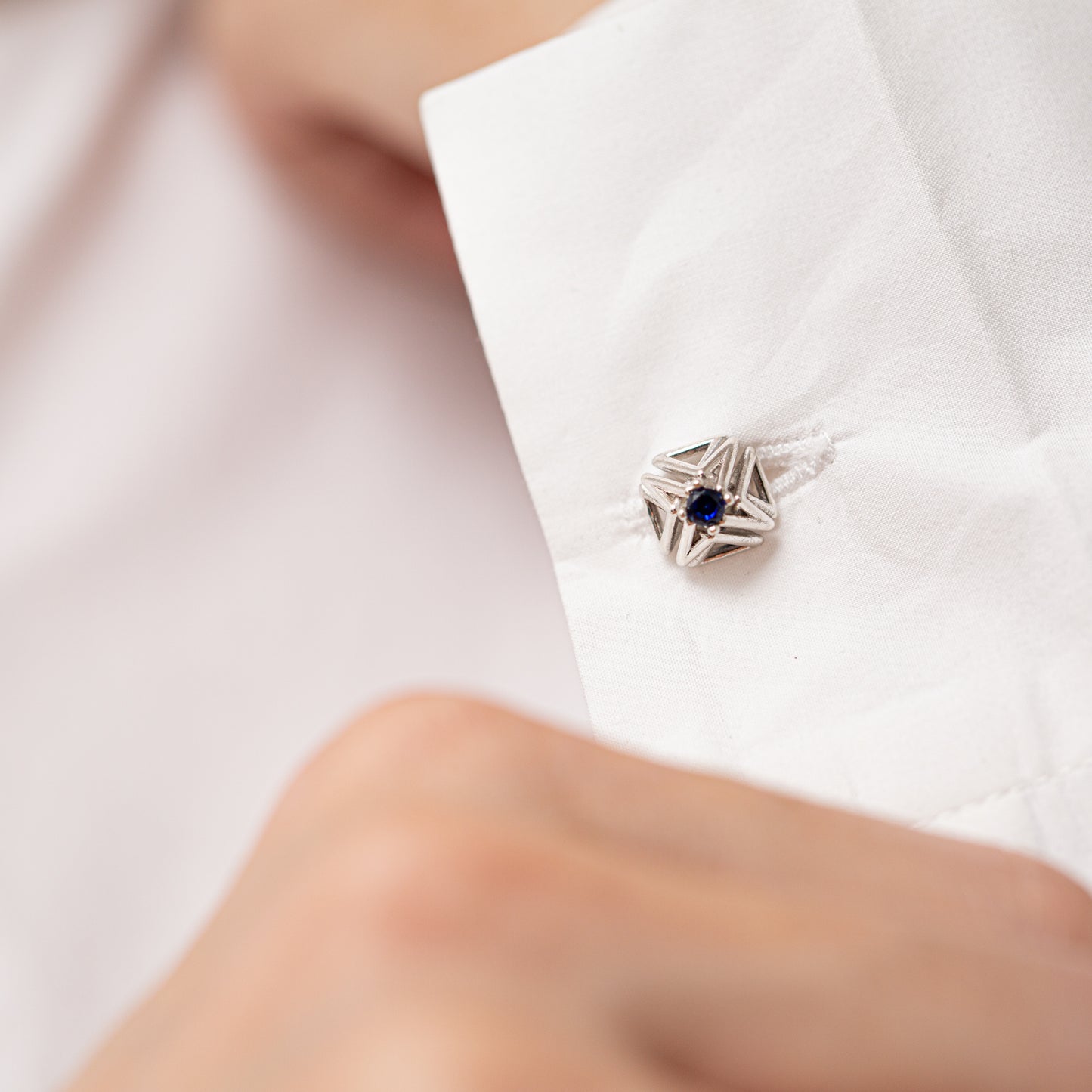 A close up of the cuff of a crisp white shirt adorned with a solid sterling silver and blue sapphire cuff link. 
