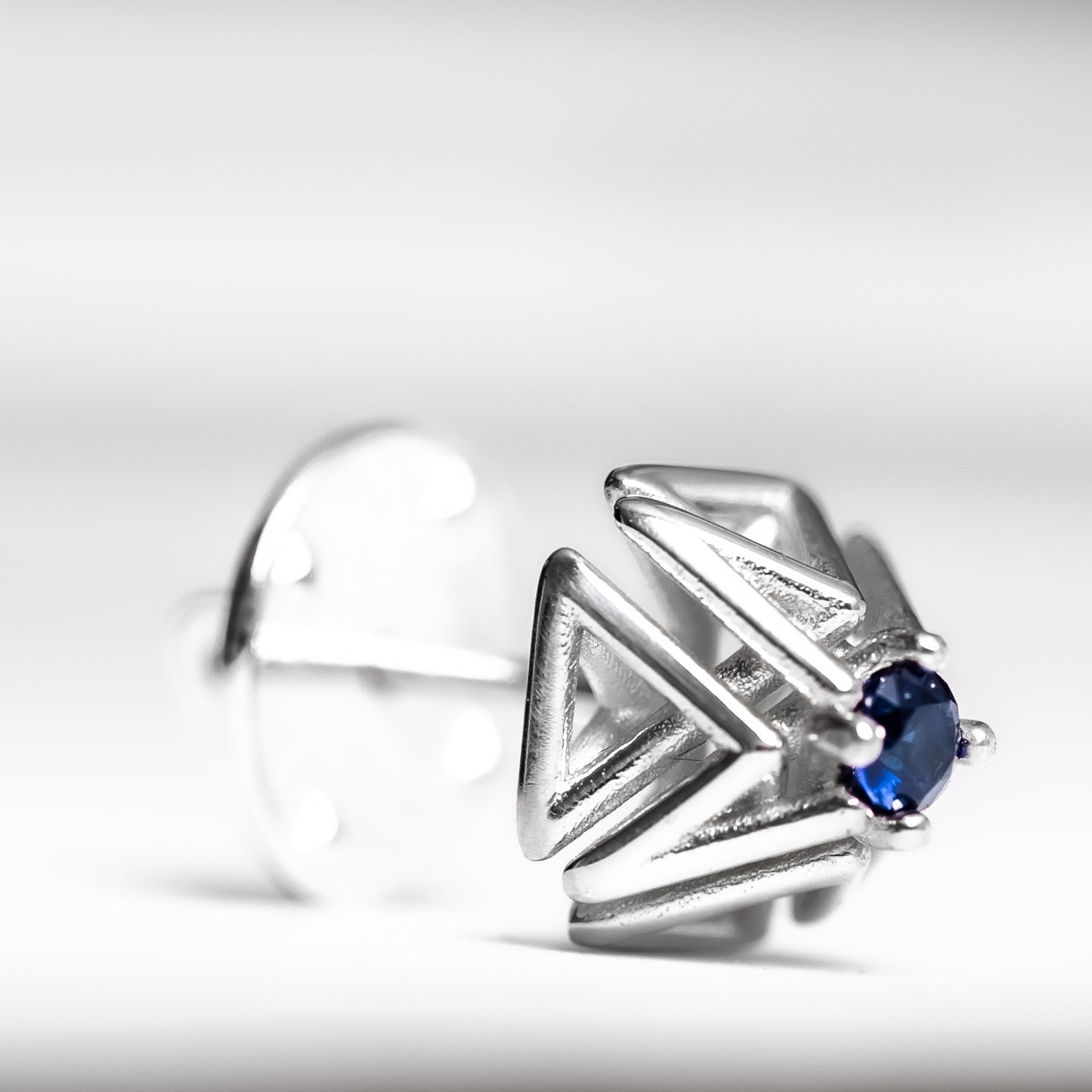 Close up shot of an intricate geometric solid .925 silver tie tack with hand set blue sapphire.