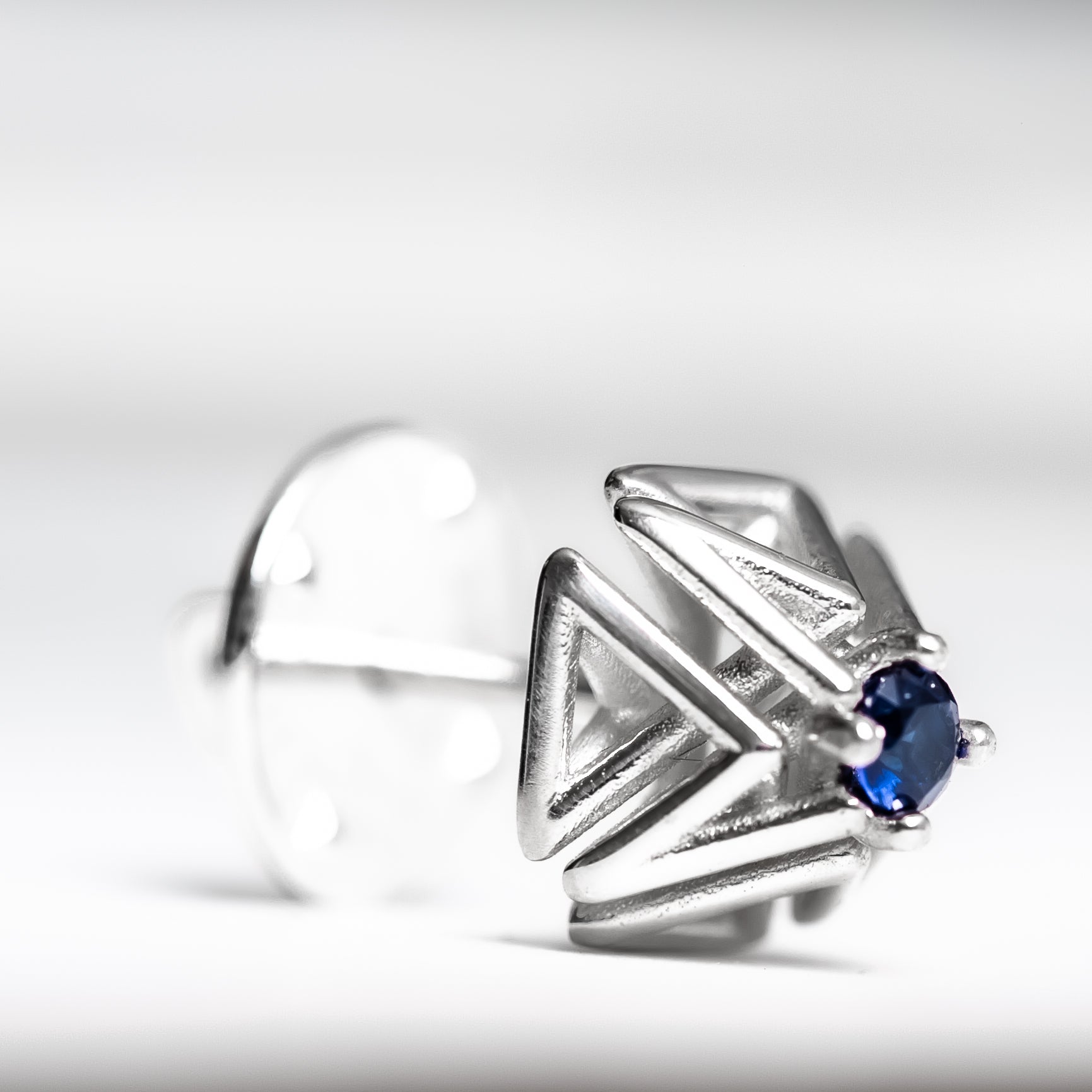 Close up shot of an intricate geometric solid .925 silver tie tack with hand set blue sapphire.