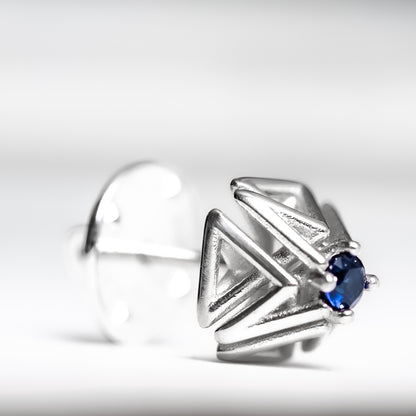 Close up shot of an intricate geometric solid .925 silver tie tack with hand set blue sapphire.