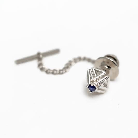 A blue sapphire and solid sterling silver tie tack with security chain rests on a white background. 
