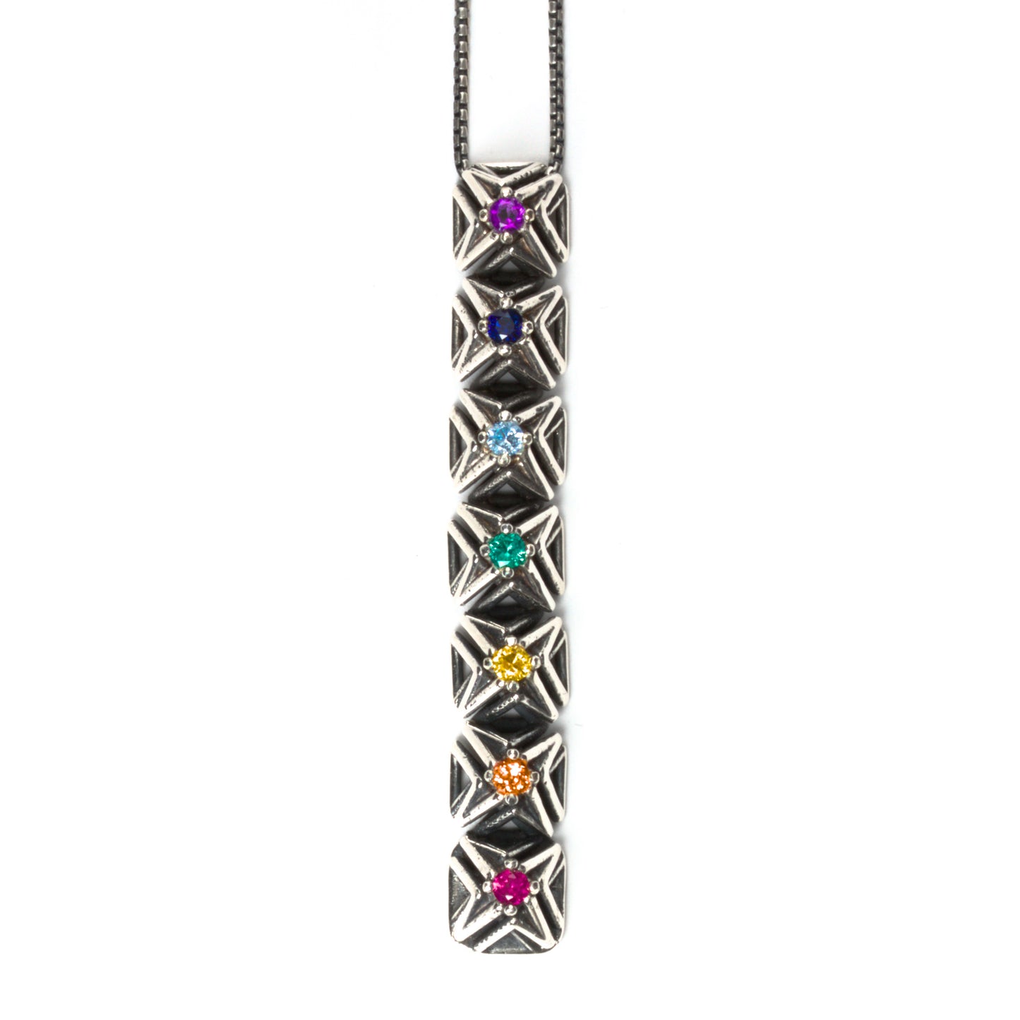 Seven rainbow colored gemstones are arranged in chakra order in this latticework bar pendant necklace. The intricate pyramid spike settings are made of contrast oxidized solid sterling silver. It is suspended from a matching box chain. 