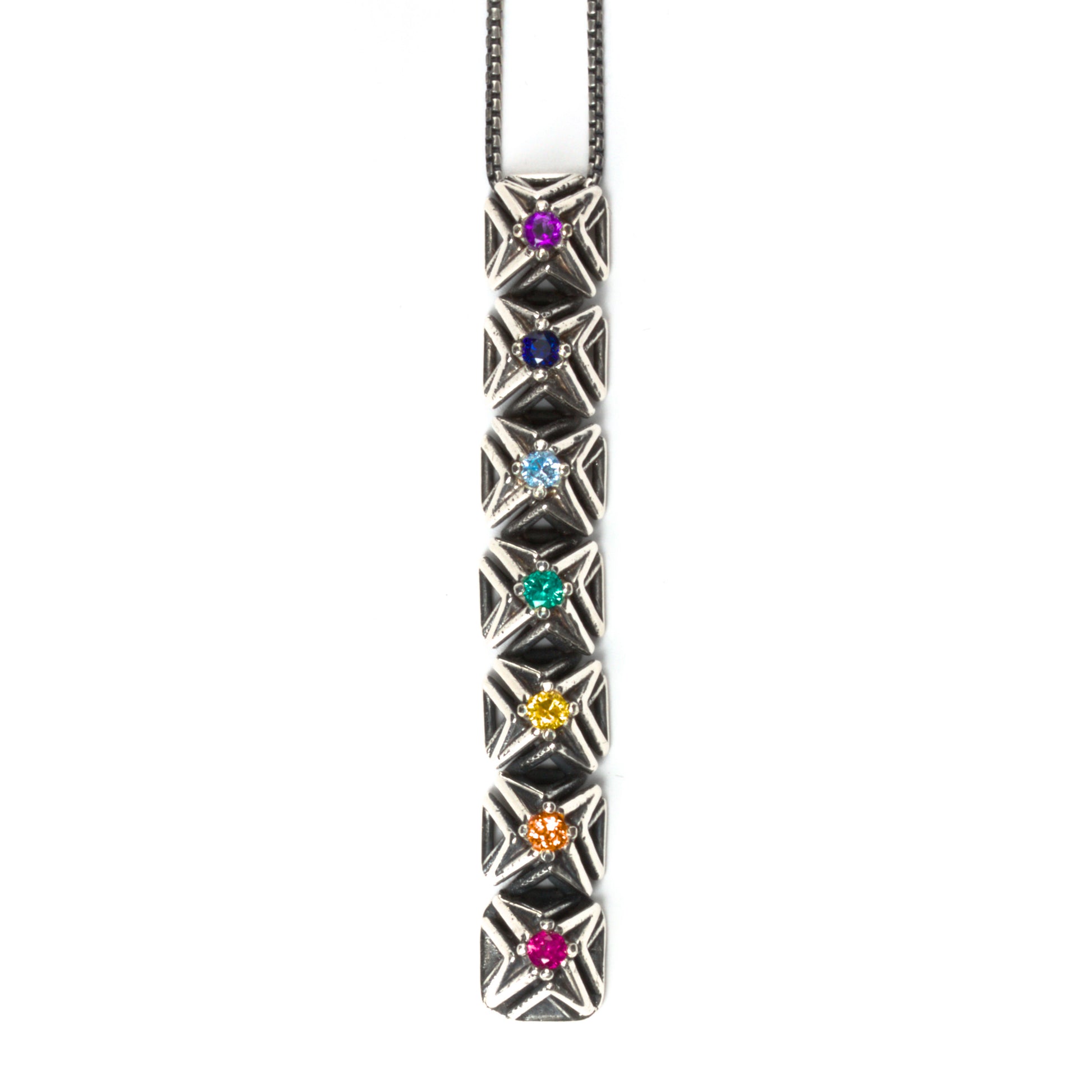 Seven rainbow colored gemstones are arranged in chakra order in this latticework bar pendant necklace. The intricate pyramid spike settings are made of contrast oxidized solid sterling silver. It is suspended from a matching box chain. 