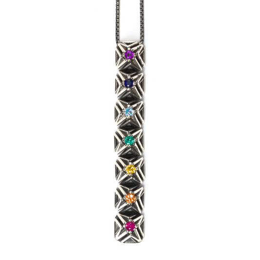 Seven rainbow colored gemstones are arranged in chakra order in this latticework bar pendant necklace. The intricate pyramid spike settings are made of contrast oxidized solid sterling silver. It is suspended from a matching box chain. 