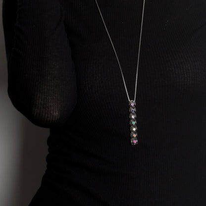 Close up of .925 sterling silver studded bar pendant set with colorful faceted gemstones. The necklace's detailed lattice stands out in edgy contrast against the black designer top it's worn with. 