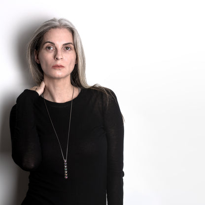 Sleek silver bar pendant with hand set colored gemstones worn with layered designer tops. A long adjustable chain secures the detailed lattice of this versatile unisex necklace. 