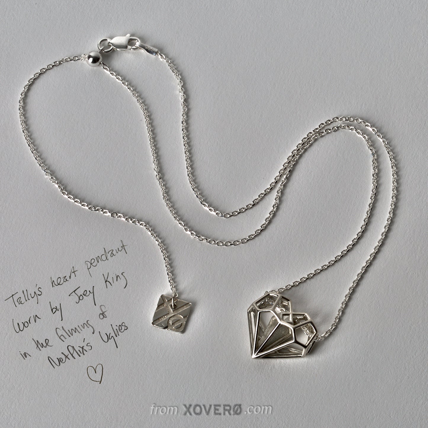 Geoheart Pendant necklace from the Netflix movie Uglies, showing the hallmark counterweight with the X/0 logo and the slider mechanism for customizable lengths. Designed by Xover0 Jewelry, this solid .925 sterling silver heart pendant merges Art Deco architecture with a modern aesthetic, emphasizing its iconic, heirloom-quality design.