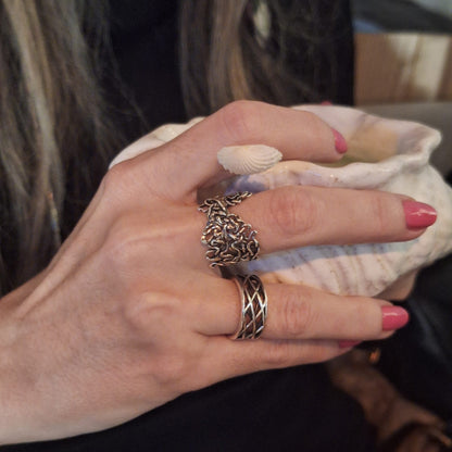 Hand wearing two silver rings with pink nail polish holding a shell. One ring features interlaced oxbows of the Mississippi River. 