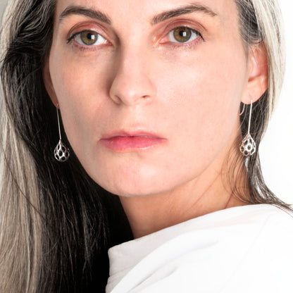 Sterling silver drop earrings with dimensional raindrop pierced by ocular cutouts reflect light from their highly polished surfaces. Photographed here on the designer, they are one of her go-to pairs of earrings for daily wear.
