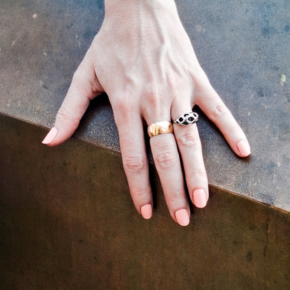 Hand wearing a sterling silver sculptural ring with puffed lattice crown next to a gold band against an edgy abstract background. 