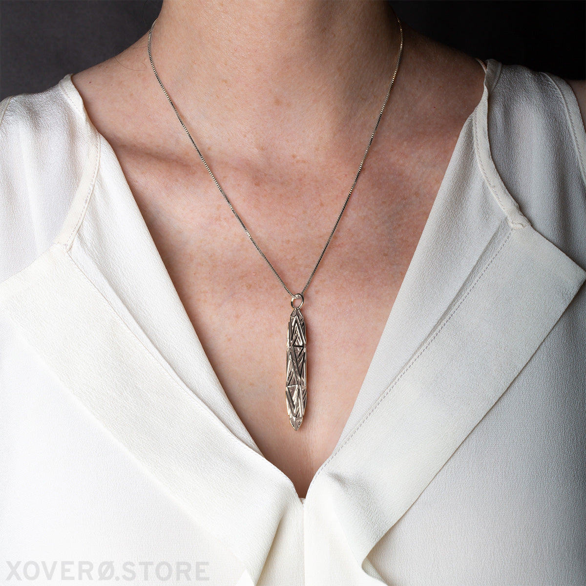 Sculptural pendant crafted from real sterling silver framed by the deep V-neck of a minimalist raw silk blouse.