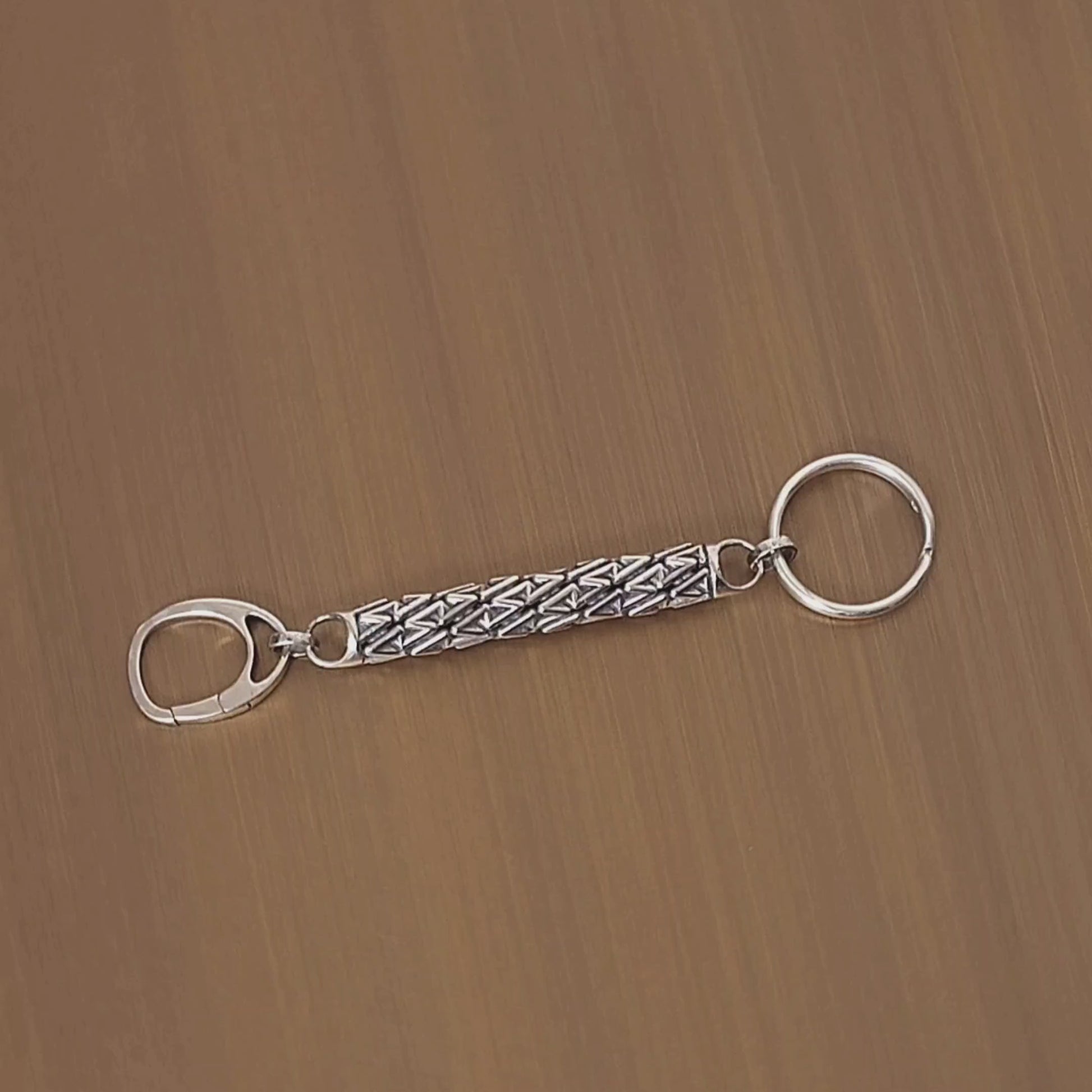 Sculptural sterling silver designer keychain revolves on a turntable, showcasing its dimensional lattice details from all angles. 