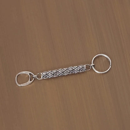 Sculptural sterling silver designer keychain revolves on a turntable, showcasing its dimensional lattice details from all angles. 
