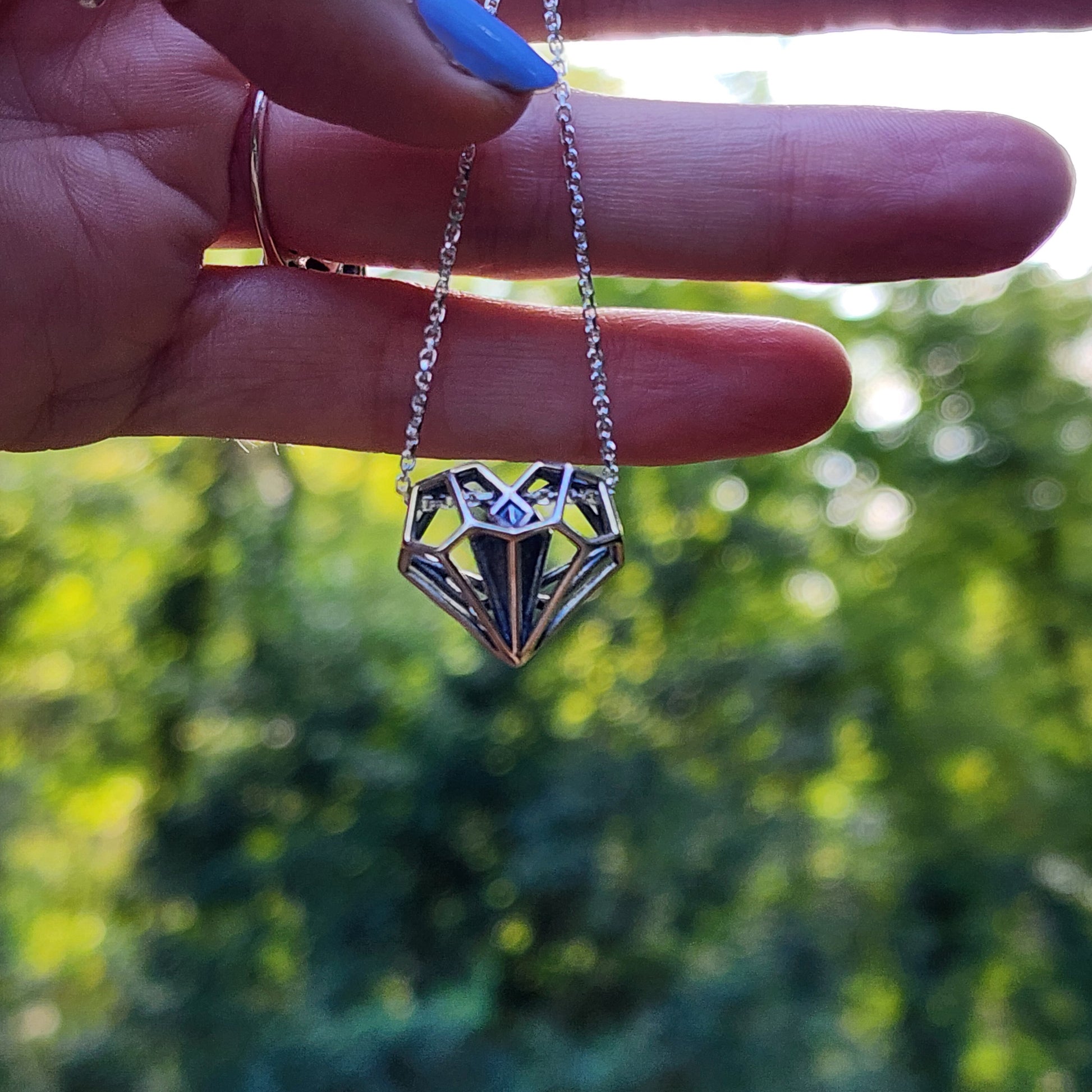 Hand holding a silver geometric heart pendant necklace in the woods during golden hour light. 