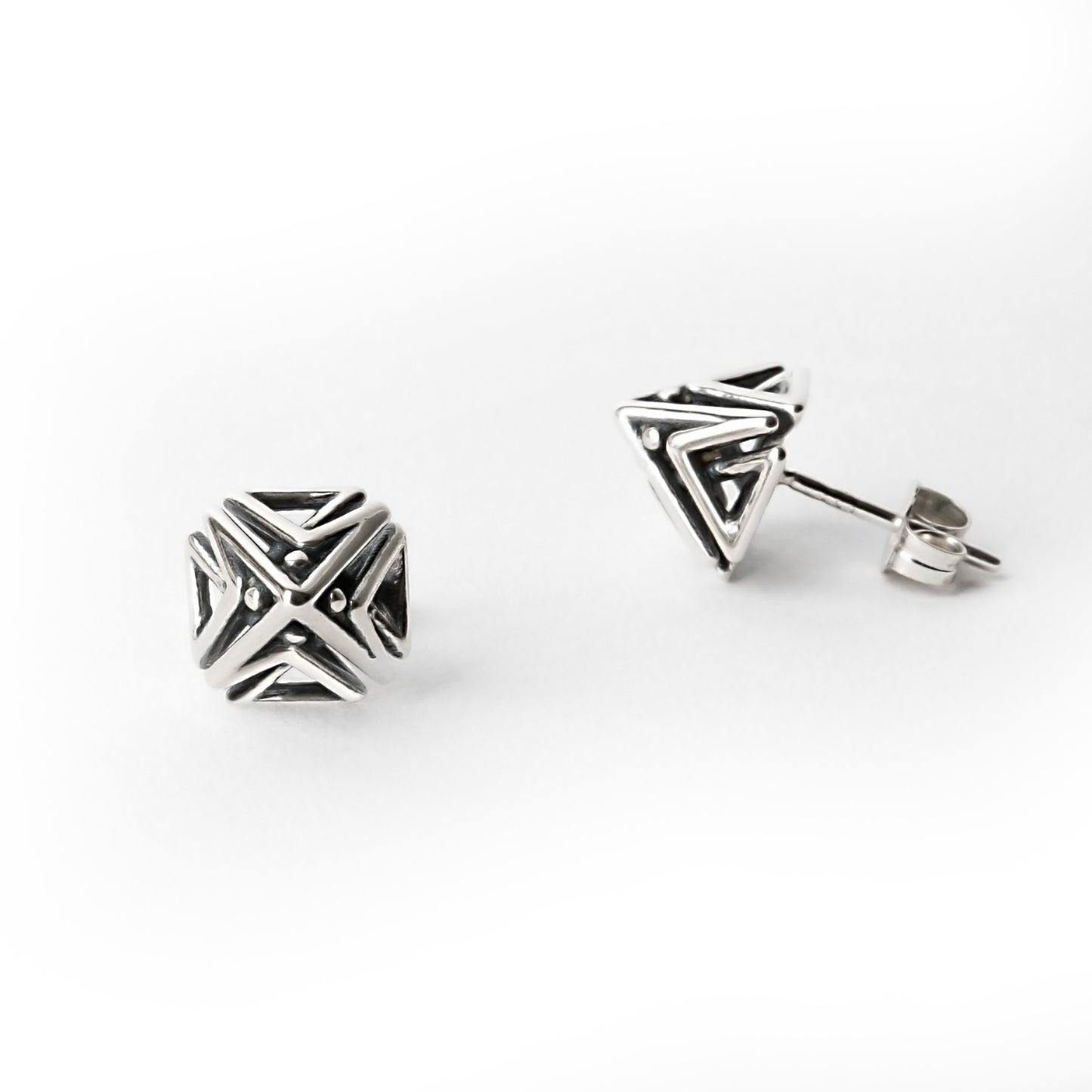 Close-up of one Doxos sterling silver pyramid stud earring shown in front view, with the other earring visible from a side profile, highlighting geometric lattice detail.