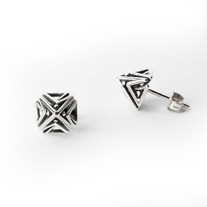 Close-up of one Doxos sterling silver pyramid stud earring shown in front view, with the other earring visible from a side profile, highlighting geometric lattice detail.