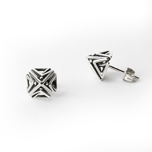 Close-up of one Doxos sterling silver pyramid stud earring shown in front view, with the other earring visible from a side profile, highlighting geometric lattice detail.