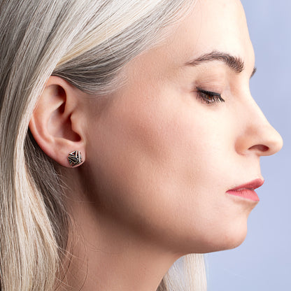 Close-up of a woman's profile with a focus on her ear and detailed pyramid stud earring against a light blue background.