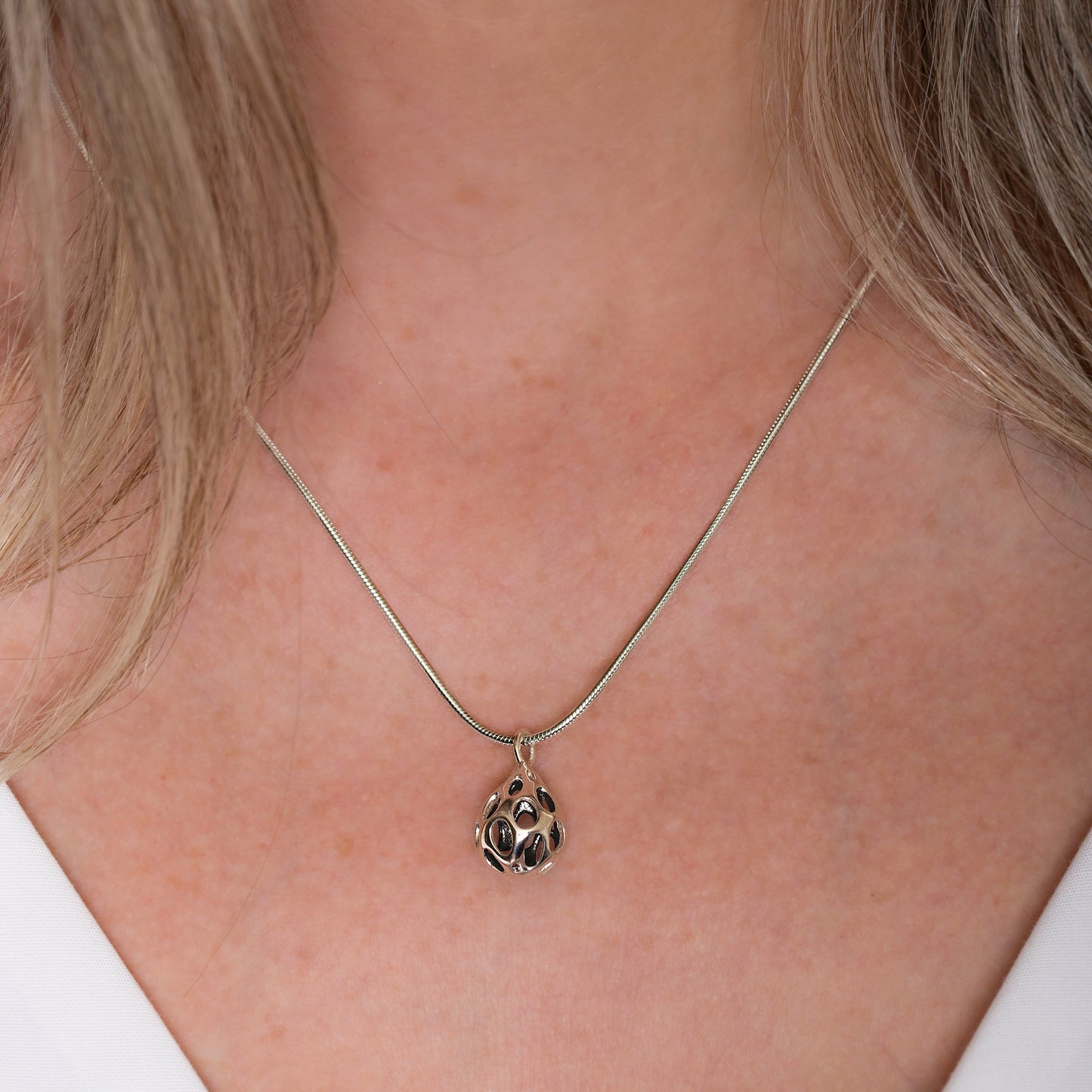 Xover0���s sterling silver OLEA pendant necklace worn at the center of a V-neck d��collet��. The dimensional teardrop design catches the light, highlighting its sculptural form and polished finish.