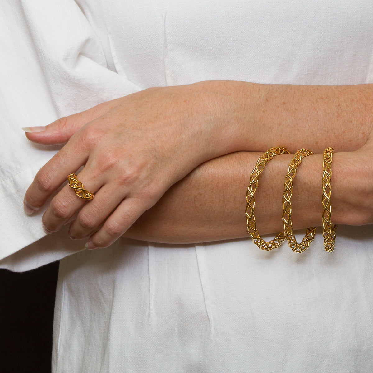 A person wearing an airy geometric ring and three stacking bangle bracelets with matching latticework design.