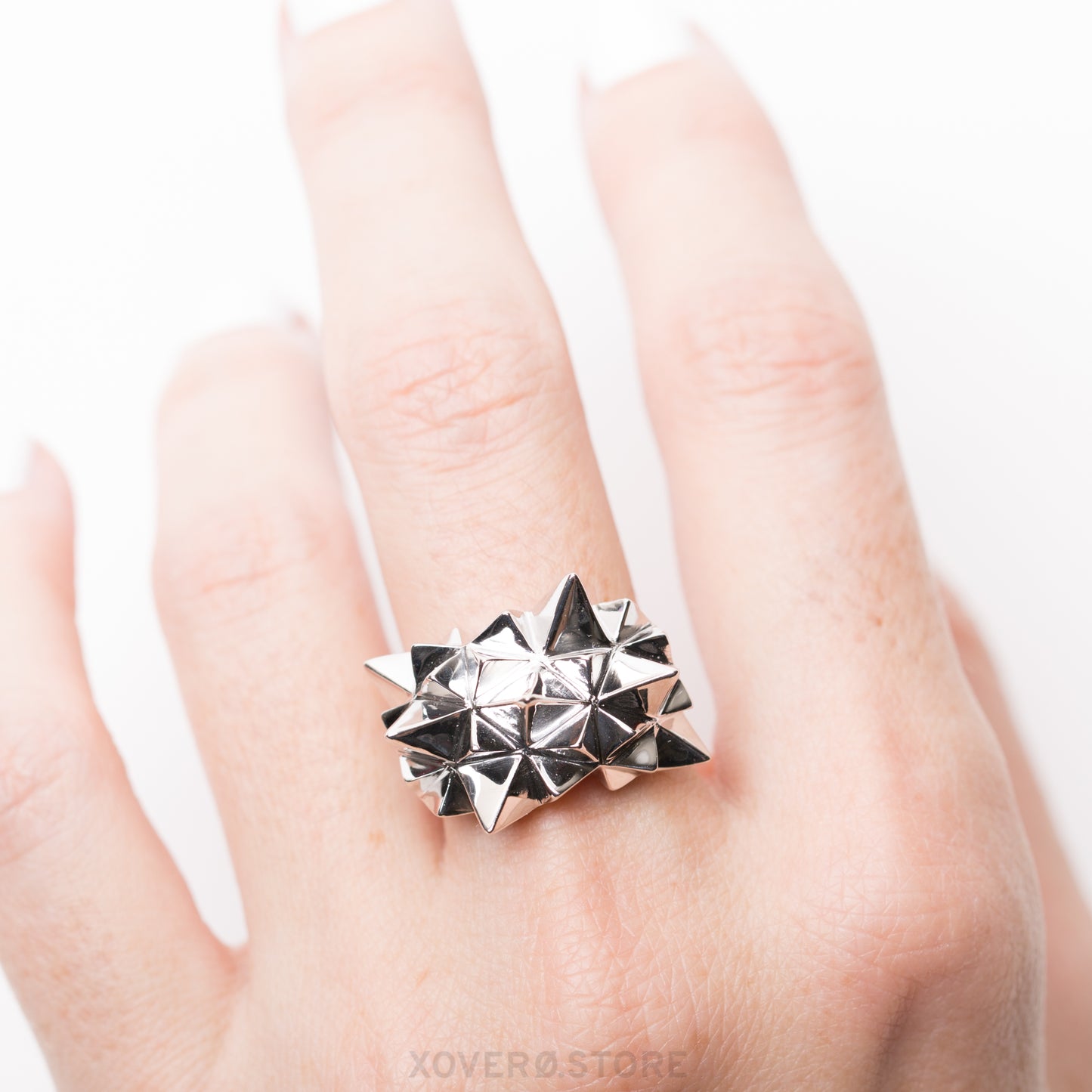 A sterling silver ring with a geometric radiating spikes design and mirror-like hand-polished finish, worn on a finger.