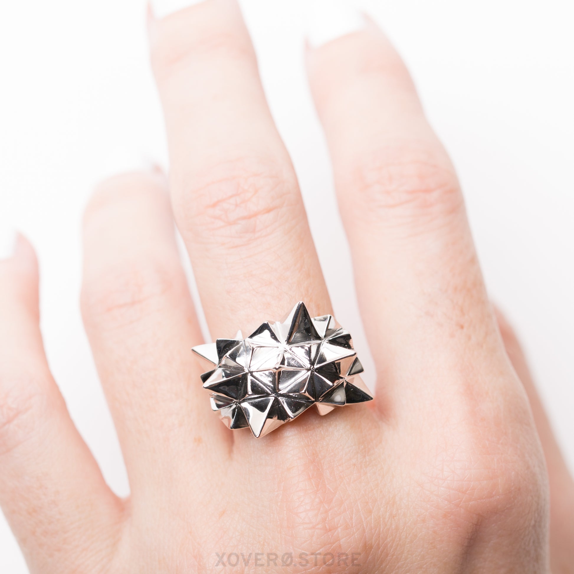 A sterling silver ring with a geometric radiating spikes design and mirror-like hand-polished finish, worn on a finger.
